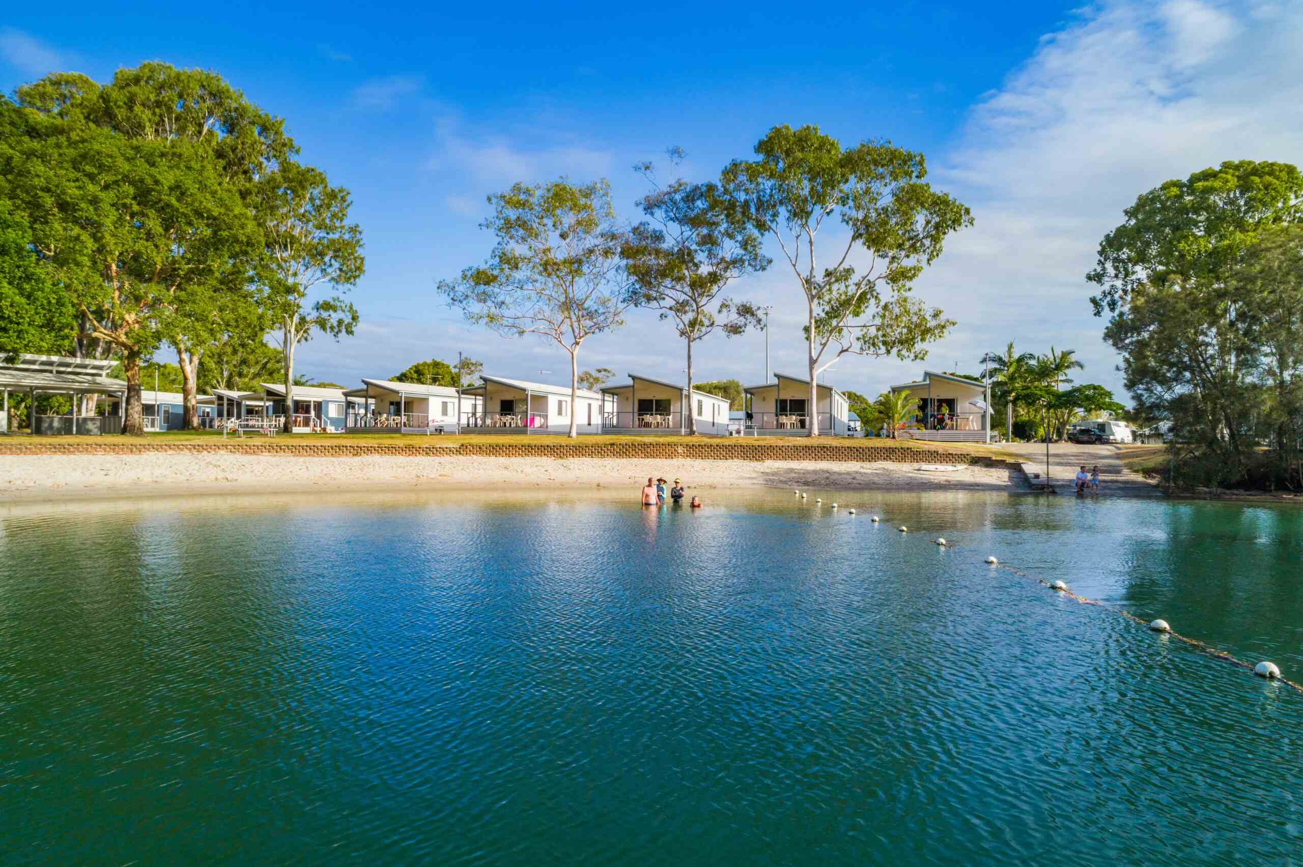 people in water and sitting on boat ramp with cabins behind them