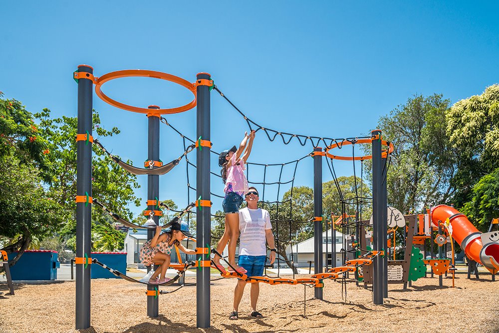 two girls climbing on the ropes in a play ground with man looking on
