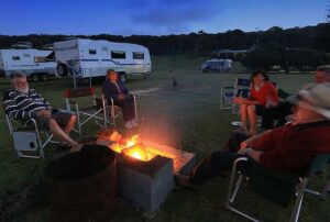 group of people sitting around a fire with caravans behind them