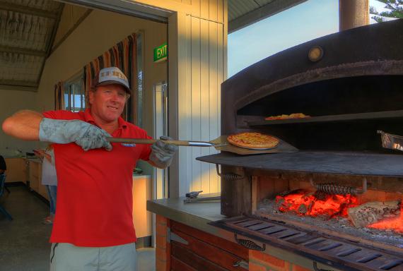 man standing before large pizza oven