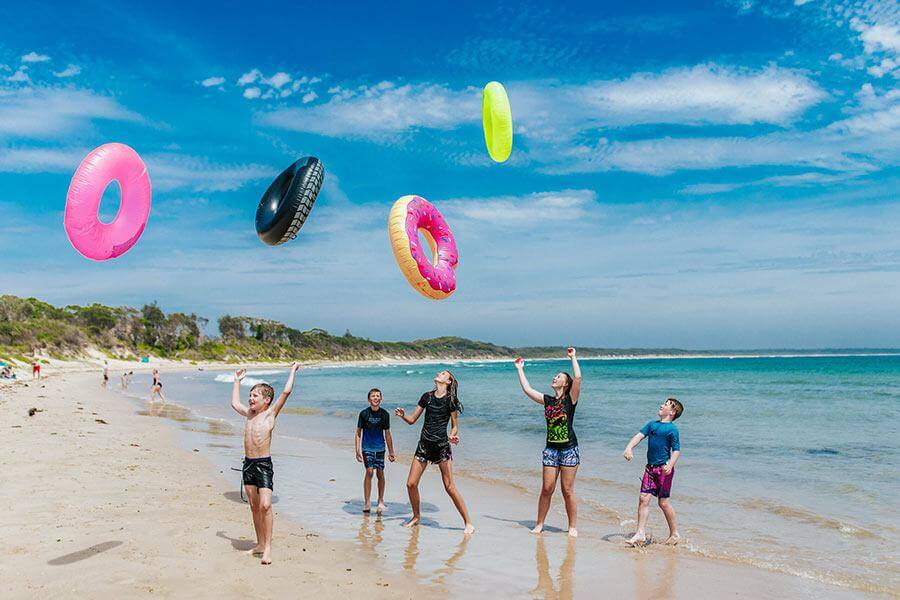 children throwing floatable donuts in the air on a beach