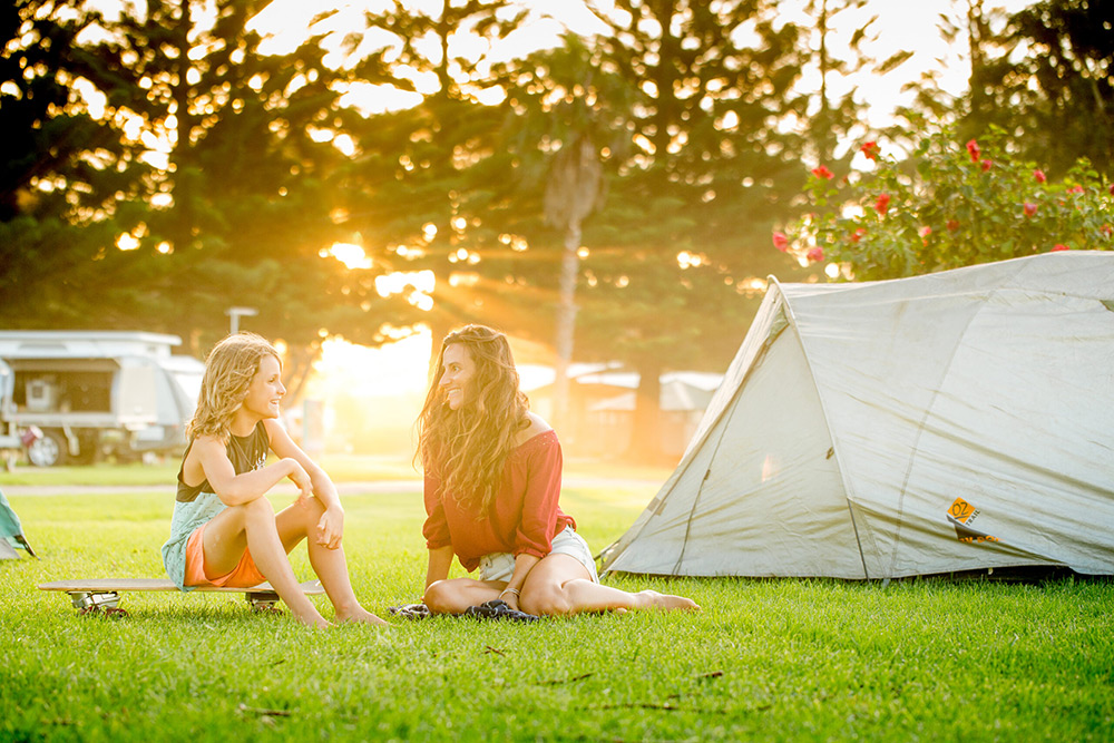 Women and a girl sitting next to a tent at sunset