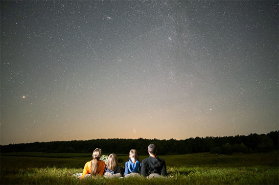 Family sitting in a field viewing the night sky