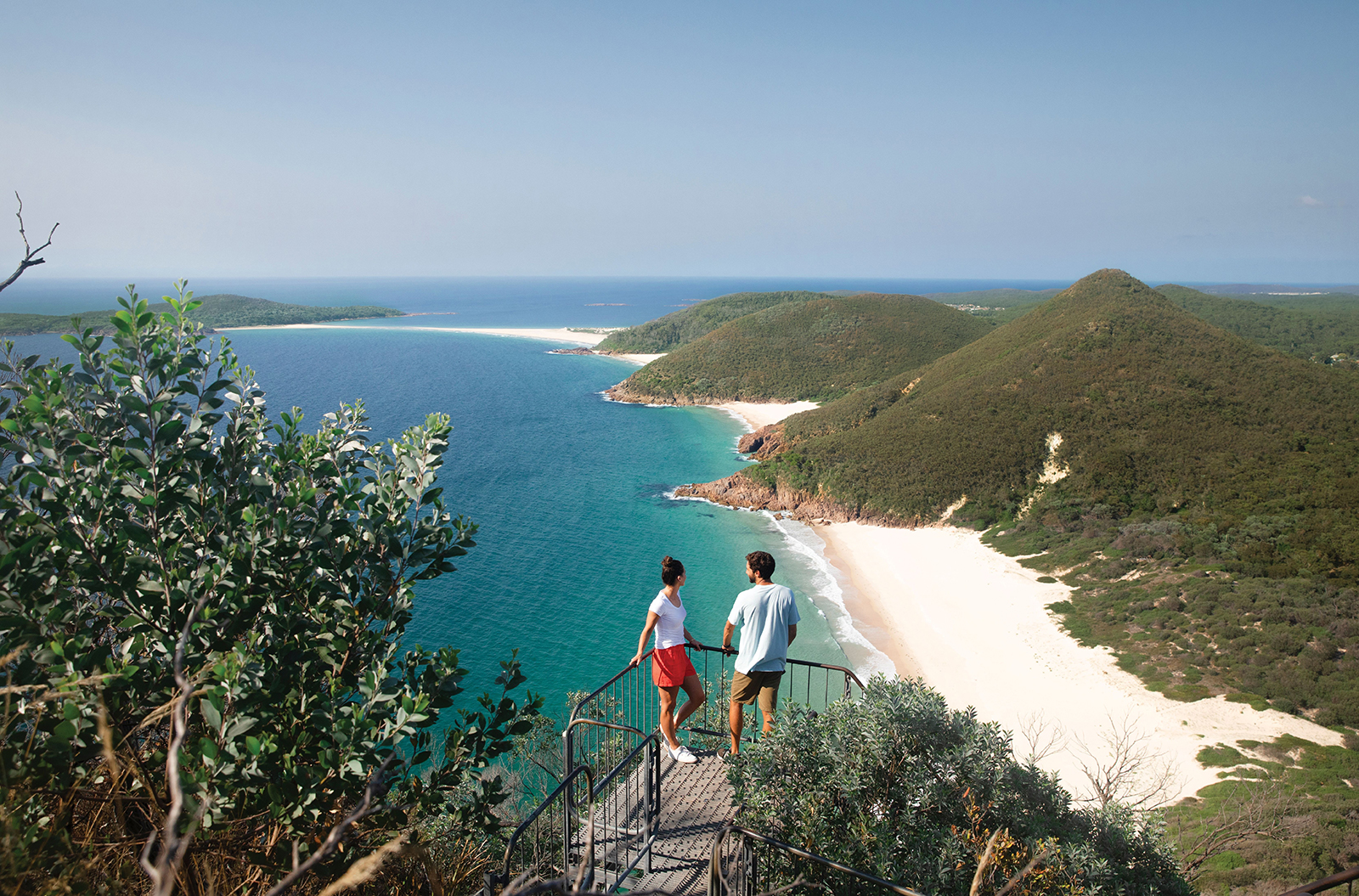 A man and a woman standing at a lookout over the ocean