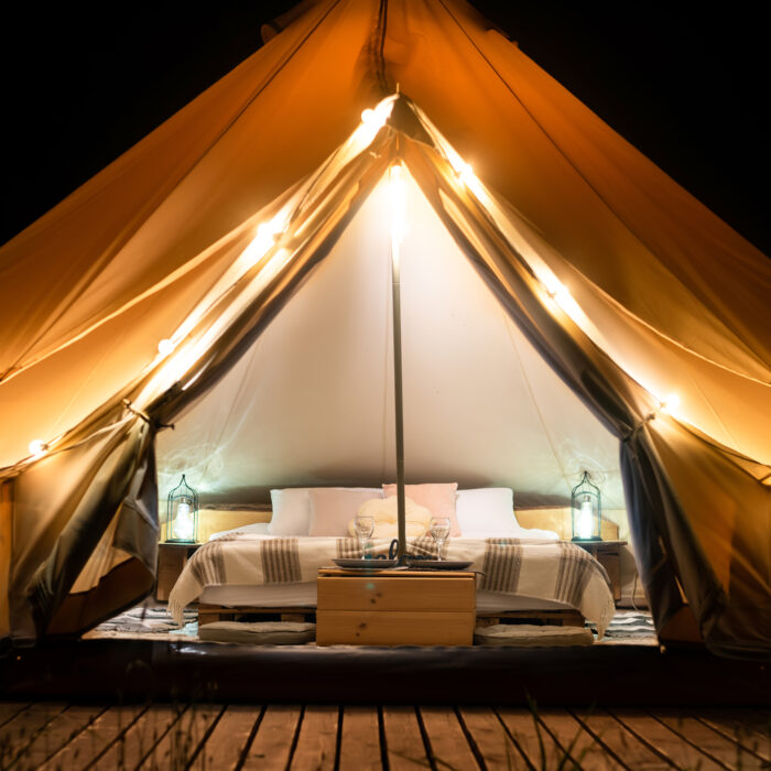 Tent interior and exterior with lamps, bed and furniture at glamping, night