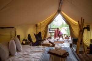 woman sitting outside luxury camping tent enjoying view of forest