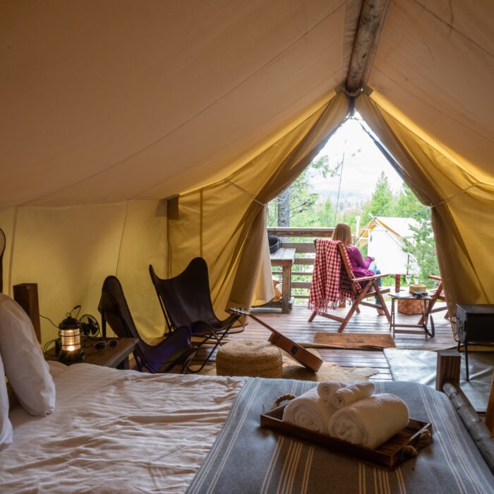 woman sitting outside luxury camping tent enjoying view of forest